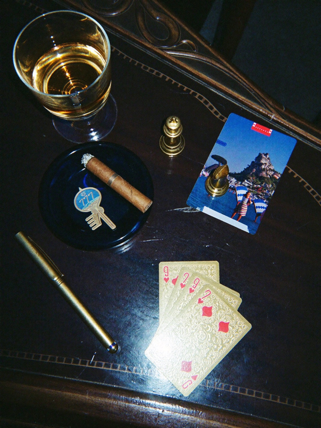 Nature morte sombre : whisky, cigare, jeu de cartes et stylo en or sur table